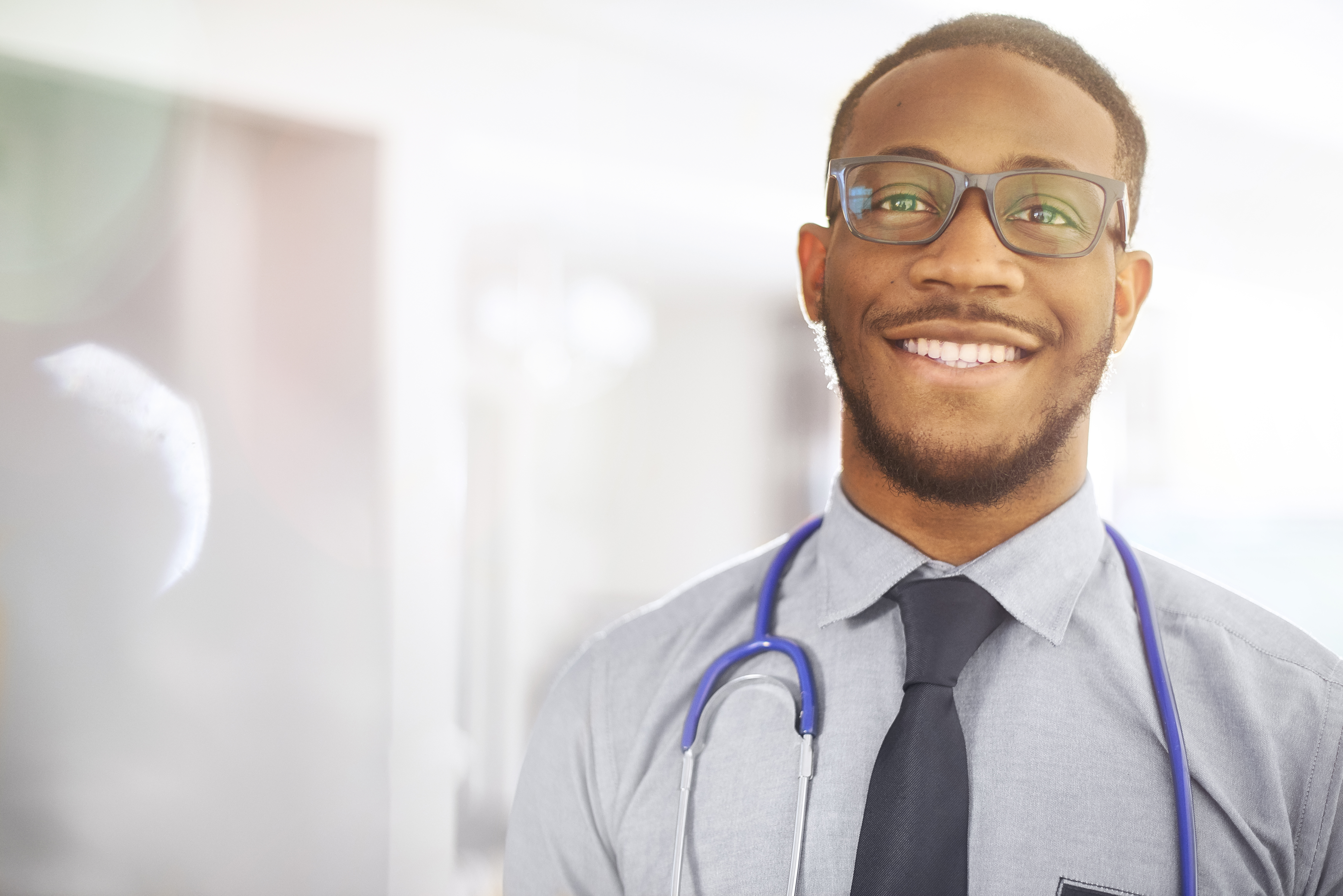 A young black junior doctor smiles to camera on ward in a hospital